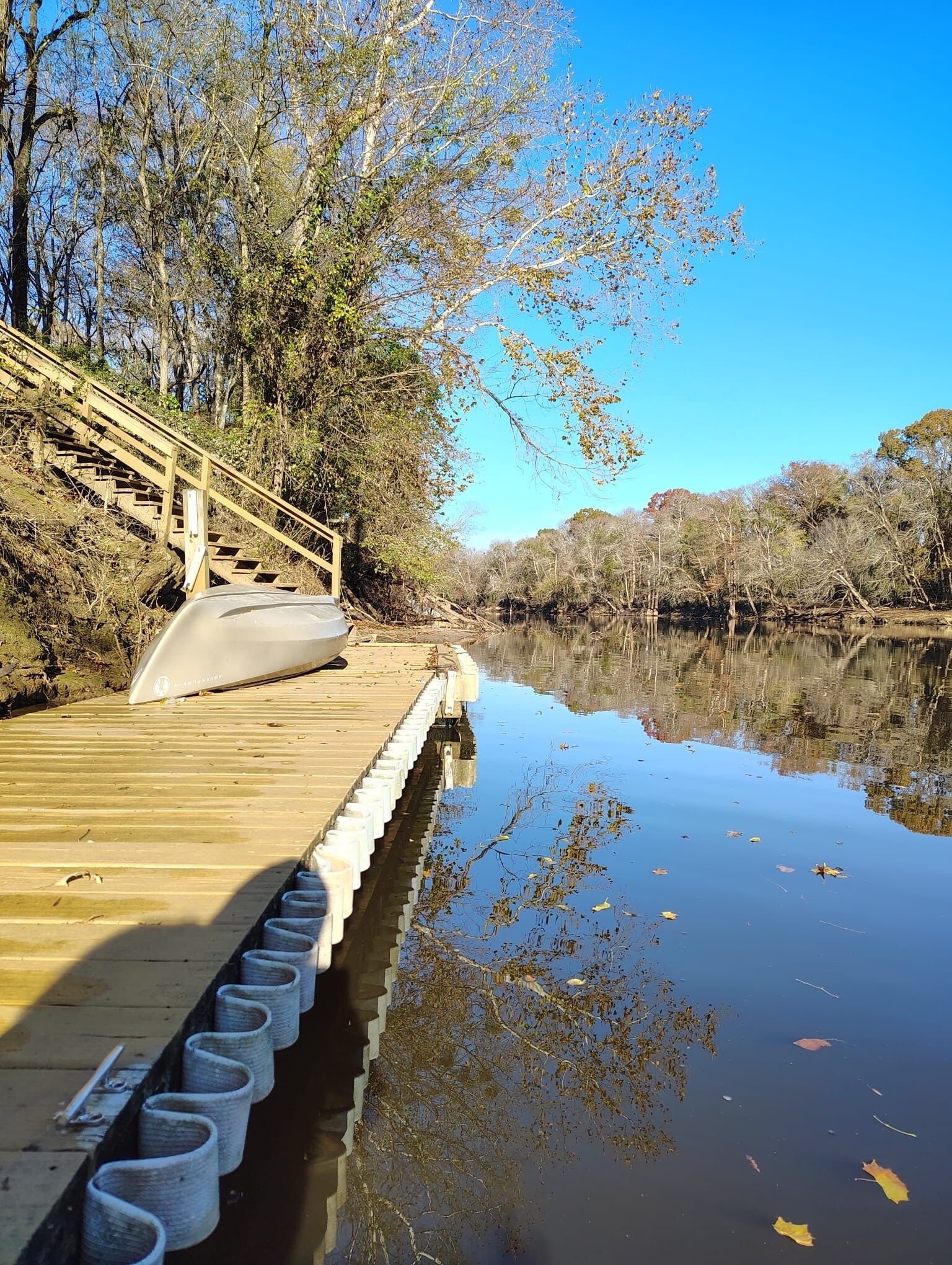 A wooden dock extending into a calm body of water, surrounded by trees and a clear sky.