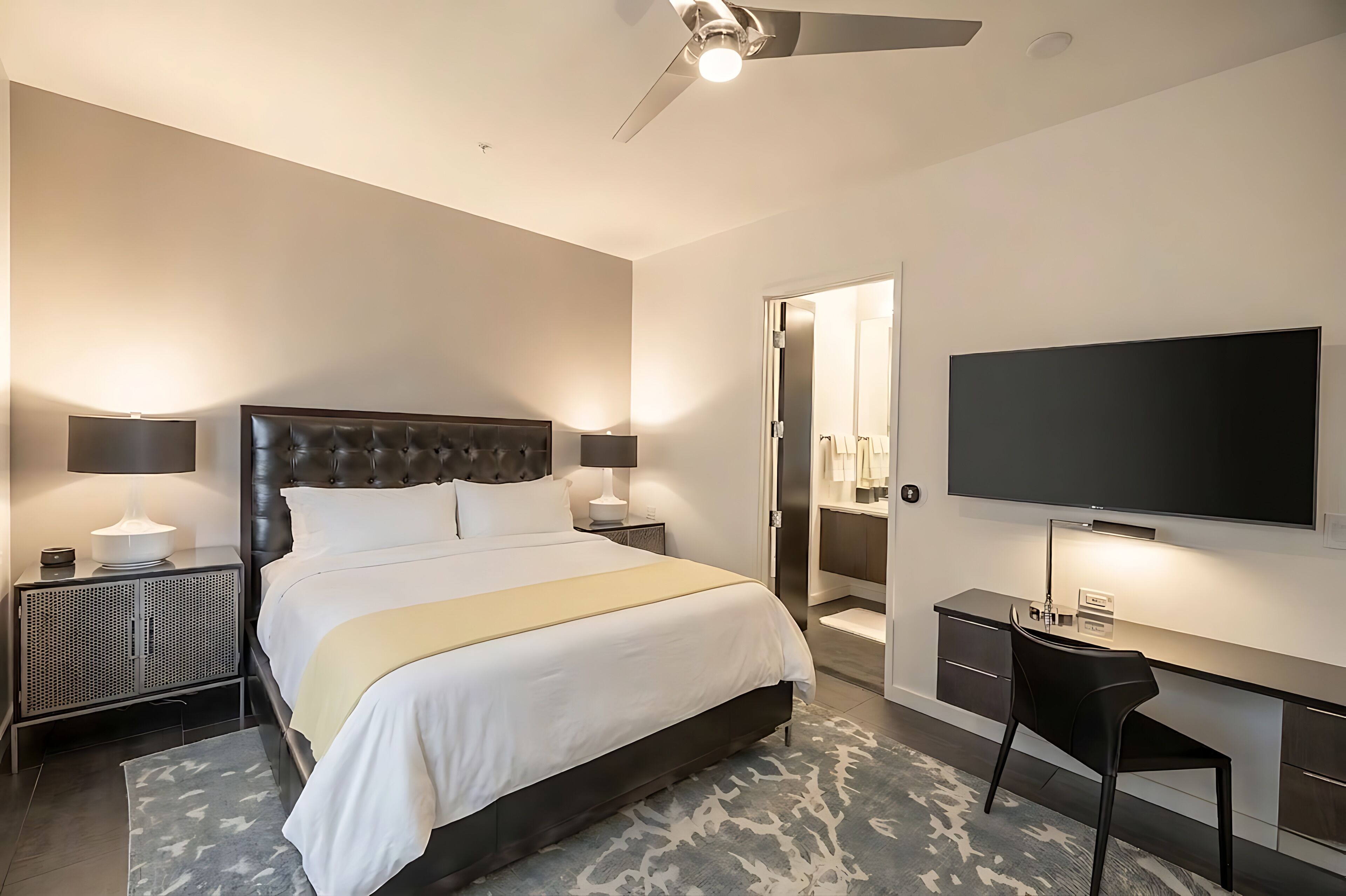 A modern hotel room with a large bed, bedside lamps, a flat-screen TV, a desk with a chair, and a walk-in closet.
