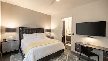 A modern hotel room with a large bed, bedside lamps, a flat-screen TV, a desk with a chair, and a walk-in closet.