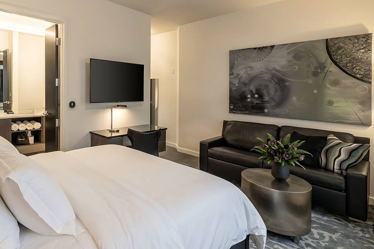 Habitació d'hotel moderna amb un llit gran, un sofà, una televisió i un quadre a la paret.