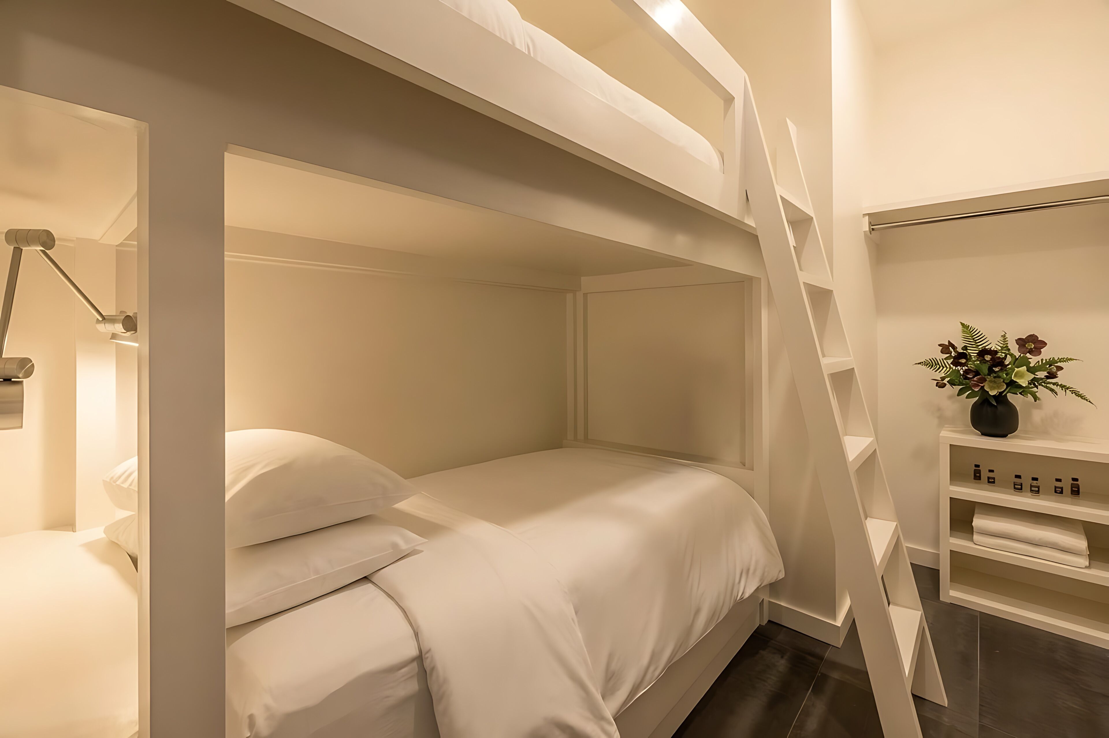 Une chambre avec un lit superposé, une échelle, une table de chevet avec une lampe et une étagère avec des articles de toilette.