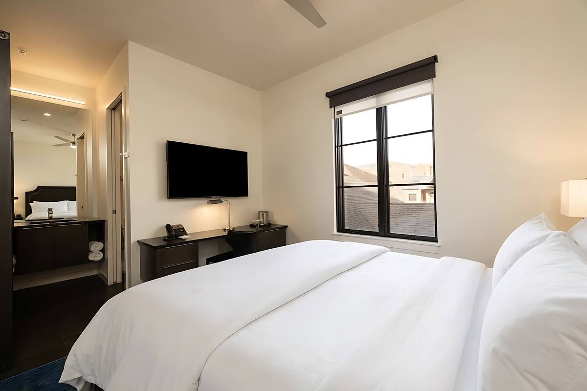 Habitació d'hotel amb llit, televisió de pantalla plana, escriptori amb làmpada, finestra amb vista i ventilador de sostre.