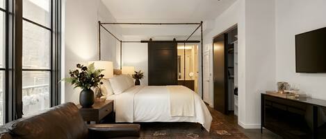 Un dormitorio con cama, mesita de noche, lámpara, planta en maceta y vistas a través de la ventana.