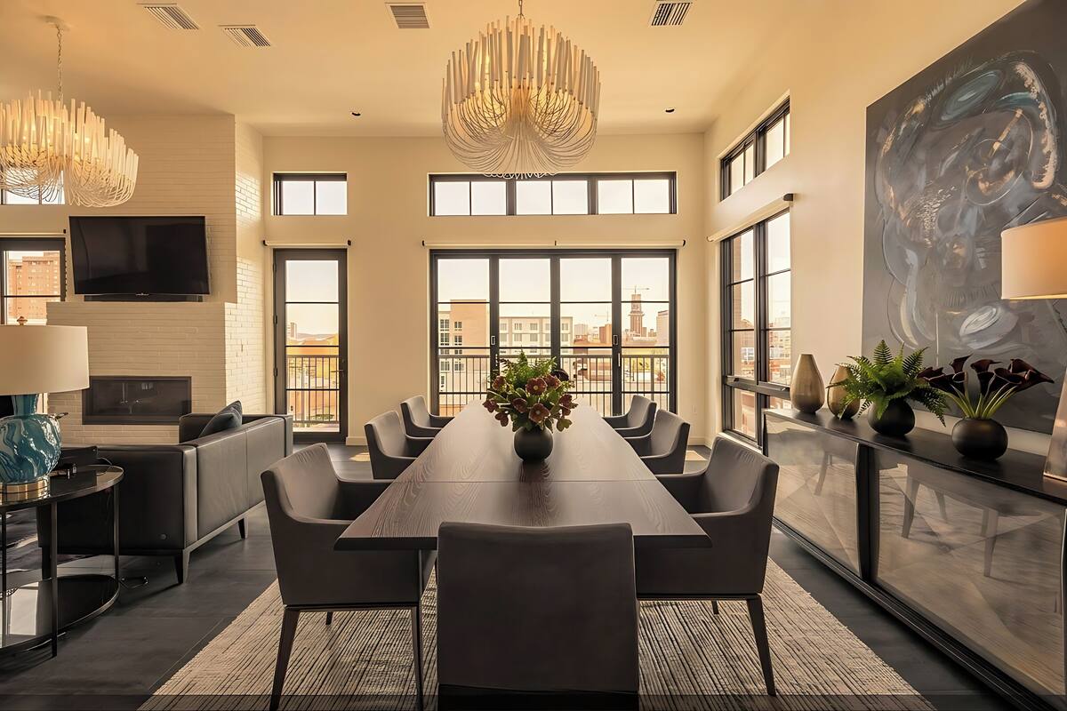 Una sala de conferències àmplia amb una taula llarga, cadires modernes, un gran finestral amb vista a la ciutat i una làmpada de cristall contemporània.