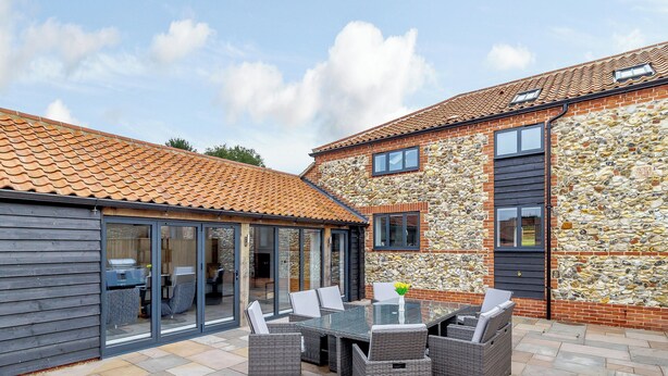 A patio area with a table and chairs, a stone wall, and a tiled roof.