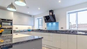 A modern kitchen with built-in appliances, a large island, pendant lighting, and a window with a view.