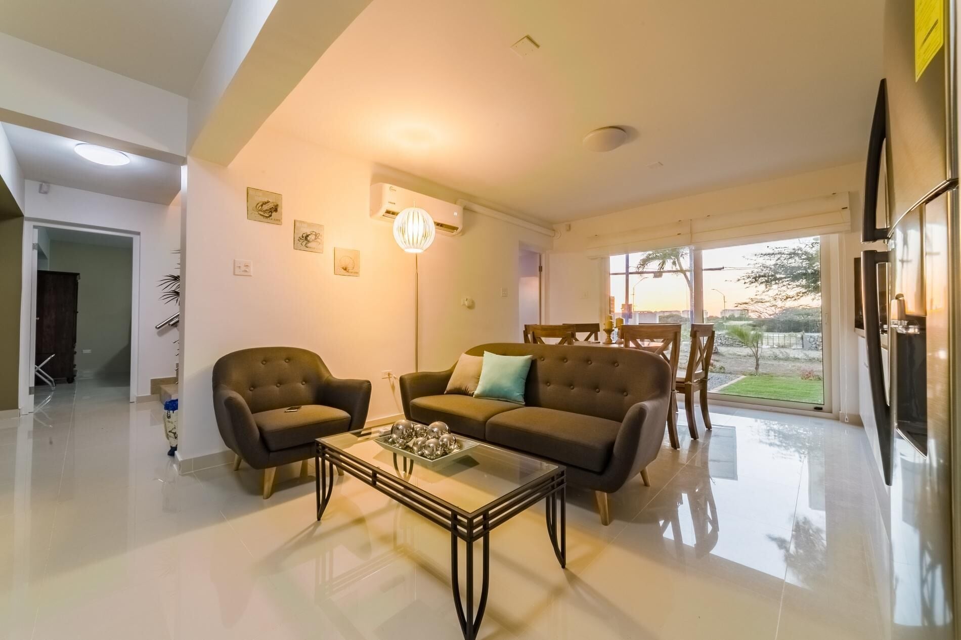 A modern living room with a glass coffee table, two sofas, and a dining area with wooden chairs.