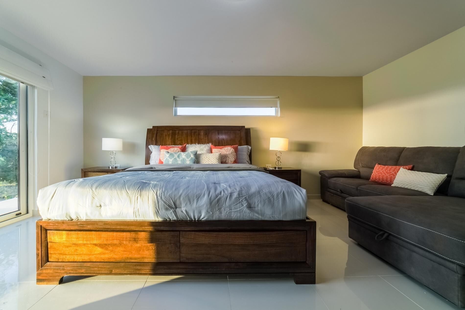 Ein modernes Schlafzimmer mit einem großen Bett, einer dunklen Couch und zwei Nachttischen mit Lampen.