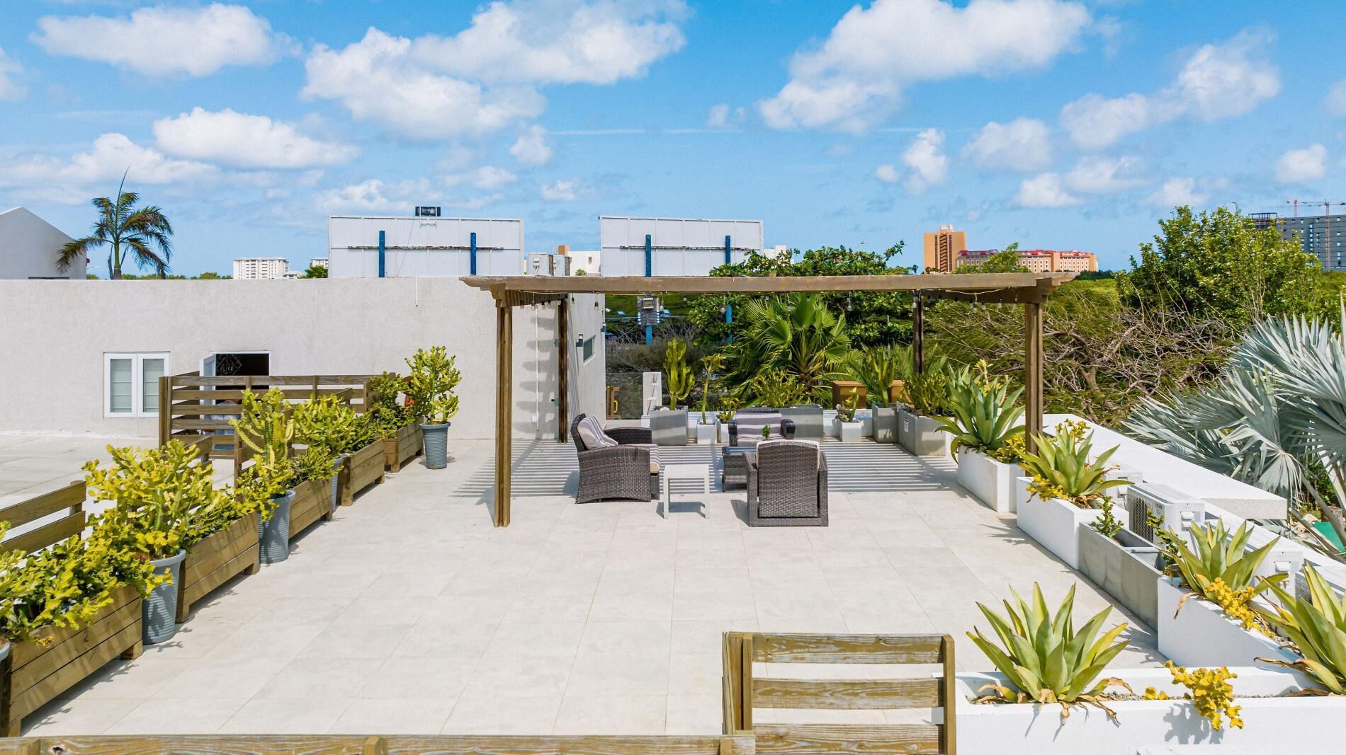 Une terrasse sur le toit avec des espaces de détente en plein air, des jardinières contenant différentes plantes et une structure en forme de pergola.