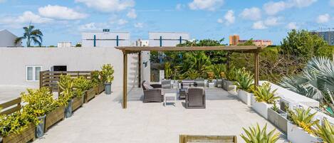 Une terrasse sur le toit avec des espaces de détente en plein air, des jardinières contenant différentes plantes et une structure en forme de pergola.