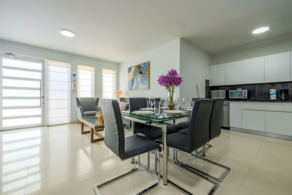 Un espace repas moderne avec une table en verre, des chaises noires et un vase rempli de fleurs violettes.
