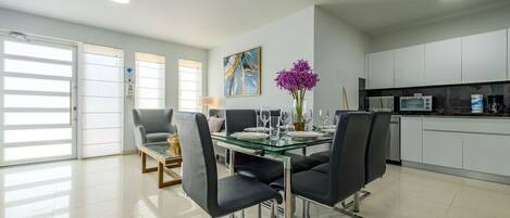Un espace repas moderne avec une table en verre, des chaises noires et un vase rempli de fleurs violettes.