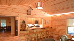 Un interior de cabaña con paredes de madera, una cocina con electrodomésticos modernos, un comedor y una zona de estar acogedora.