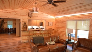 Un interior de cabaña acogedor con techo de madera, un sofá de cuero, una zona de comedor y una cocina.