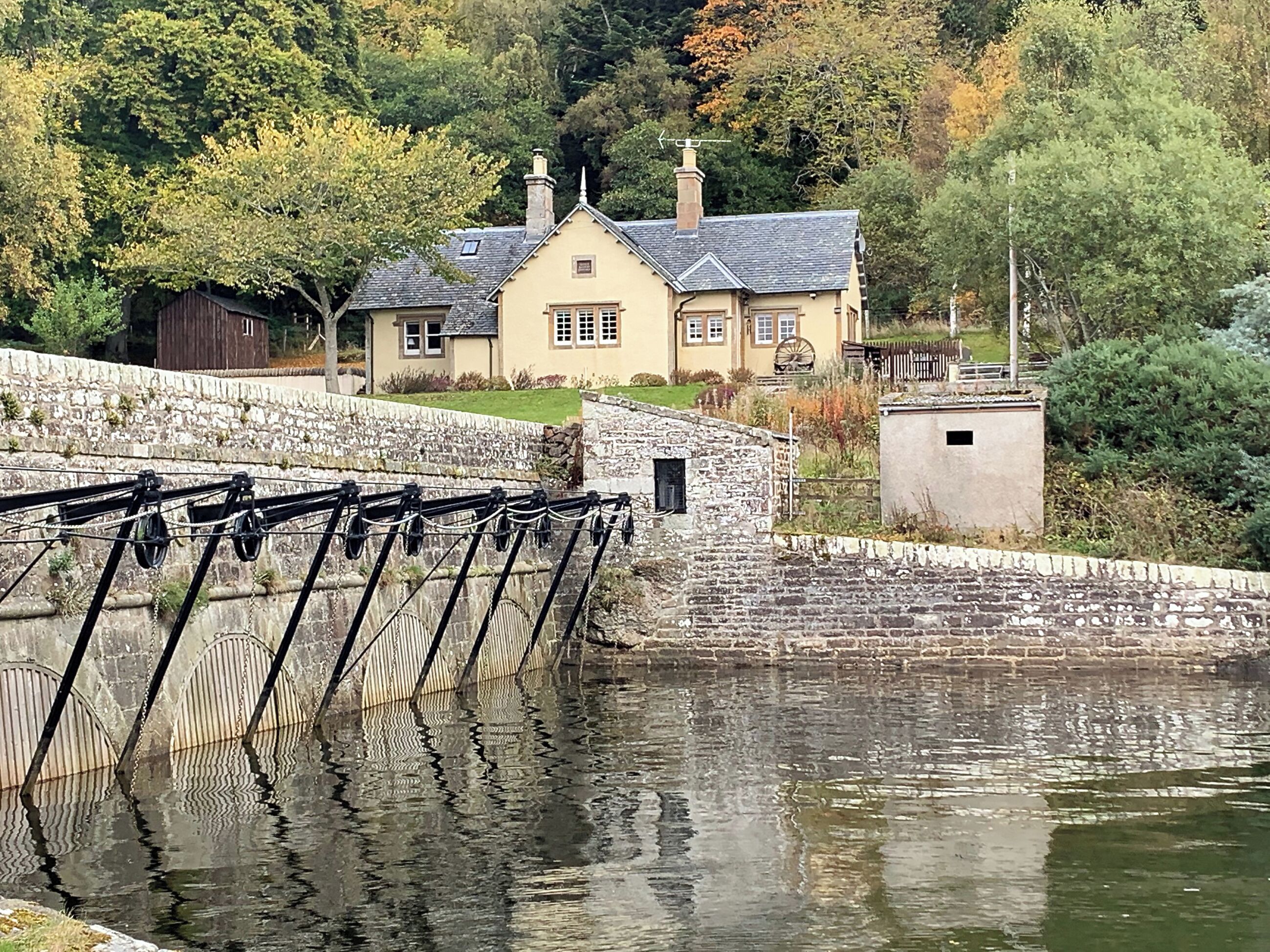 Ein steinernes Fallgitter über einem Kanal, im Hintergrund ein Haus.