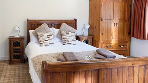 A wooden bed with a plaid floor, two bedside tables with lamps, and a wooden wardrobe. - Sluice Keeper's Cottage (Dornoch)