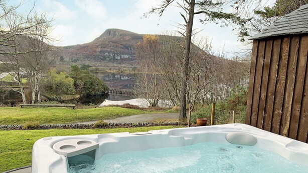 A hot tub with a view of a mountain and a wooden fence. - Sluice Keeper's Cottage (Dornoch)