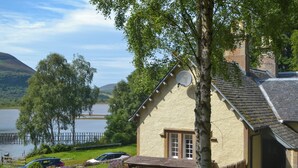A house with a satellite dish, a wooden deck, and a view of a lake and hills. - Sluice Keeper's Cottage (Dornoch)