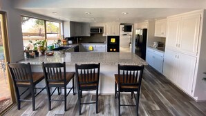 A modern kitchen with white cabinets, a granite countertop, and a central island with four chairs. - Chalet-style Home Perfect for Family - Heated Pool (Simi Valley)
