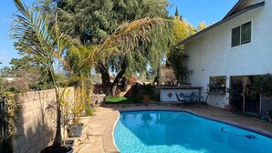 A swimming pool with a curved edge, surrounded by a concrete deck and a stone wall. - Chalet-style Home Perfect for Family - Heated Pool (Simi Valley)