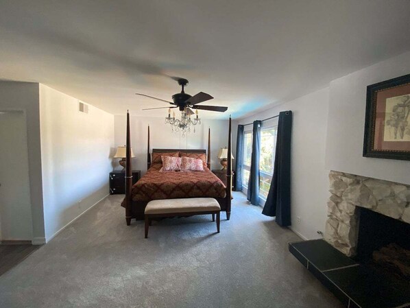 A bedroom with a four-poster bed, a stone fireplace, and a ceiling fan.