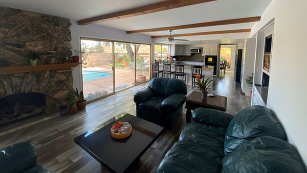 A spacious living room with a stone fireplace, a large window, and a view of the outdoor pool. - Chalet-style Home Perfect for Family - Heated Pool (Simi Valley)