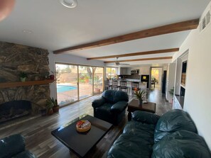 A spacious living room with a stone fireplace, a large window, and a view of the outdoor pool.