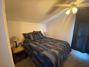 A bedroom with a bed, a nightstand, a lamp, and a ceiling fan.