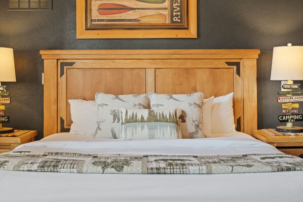 A bed with a wooden headboard, white bedding, and decorative pillows with forest and wildlife prints. - Walk-in Log Cabin with Walk-in Shower - Only Minutes from Shows! (Branson)