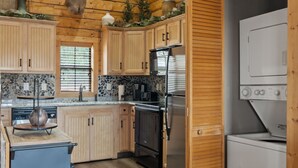 A rustic kitchen with wooden cabinets, a refrigerator, a stove, and a clock on the wall.