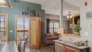 A dining area with a wooden table and chairs, a wooden cabinet with decorative items, and a view of the outdoors through a door.