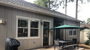 Een huis met een overdekte patio, een barbecue en een tafel met stoelen.