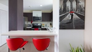 A modern kitchen with a white countertop, two red chairs, and a painting of a bridge. - The Brompton's @ Home (Kingston)