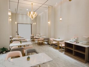 Une pièce moderne et bien éclairée, dotée d’un sol en marbre, de plusieurs tables et chaises, ainsi que d’un grand tableau blanc mural.