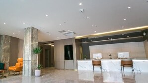 A modern lobby with marble flooring, a reception desk, and two seating areas with chairs. - Greentree Inn (Nanjing)
