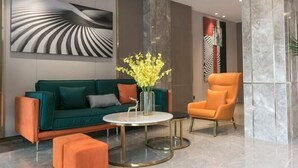 A modern lobby with a green sofa, orange armchair, and a round table with a vase of flowers. - Greentree Inn (Nanjing)