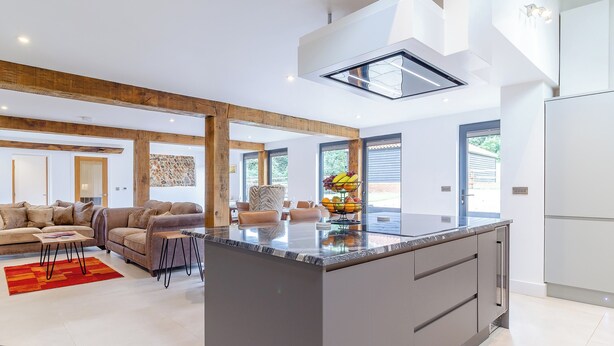 Una cocina moderna con una isla central, un comedor con sofá y sillas, y una sala de estar con un ventanal grande.