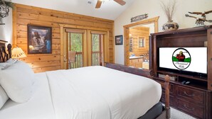 Un dormitorio con cama, paredes de madera, ventilador de techo, televisor y un cartel de bienvenida.