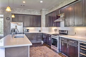 A modern kitchen with dark cabinets, stainless steel appliances, and pendant lighting.