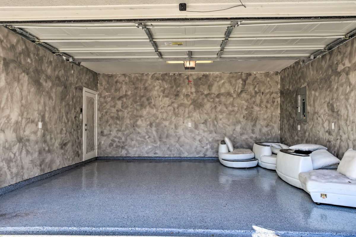 Una habitació àmplia amb un sòl de formigó polit, un sostre blanc i una paret amb textura. Hi ha zones d'seure amb seients blans i coixins, i una taula petita.