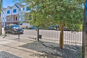 A residential street with houses, a tree, and a gated parking area.