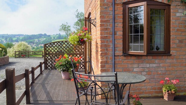 A patio with a table and chairs, a wooden fence, and potted plants. - 1 bedroom accommodation in Tregynon (Tregynon)