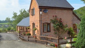 A brick building with a sloped roof, a satellite dish, and a wooden fence. - 1 bedroom accommodation in Tregynon (Tregynon)