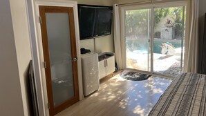 Ein Zimmer mit einer Schiebetür zu einem Poolbereich, einem an der Wand montierten Fernseher und einem kleinen Kühlschrank.