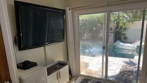 Ein Zimmer mit einem Flachbildfernseher, einem kleinen Kühlschrank, einem Schrank und einer Glastür, die zu einem Poolbereich mit Schwimmspielzeug führt.