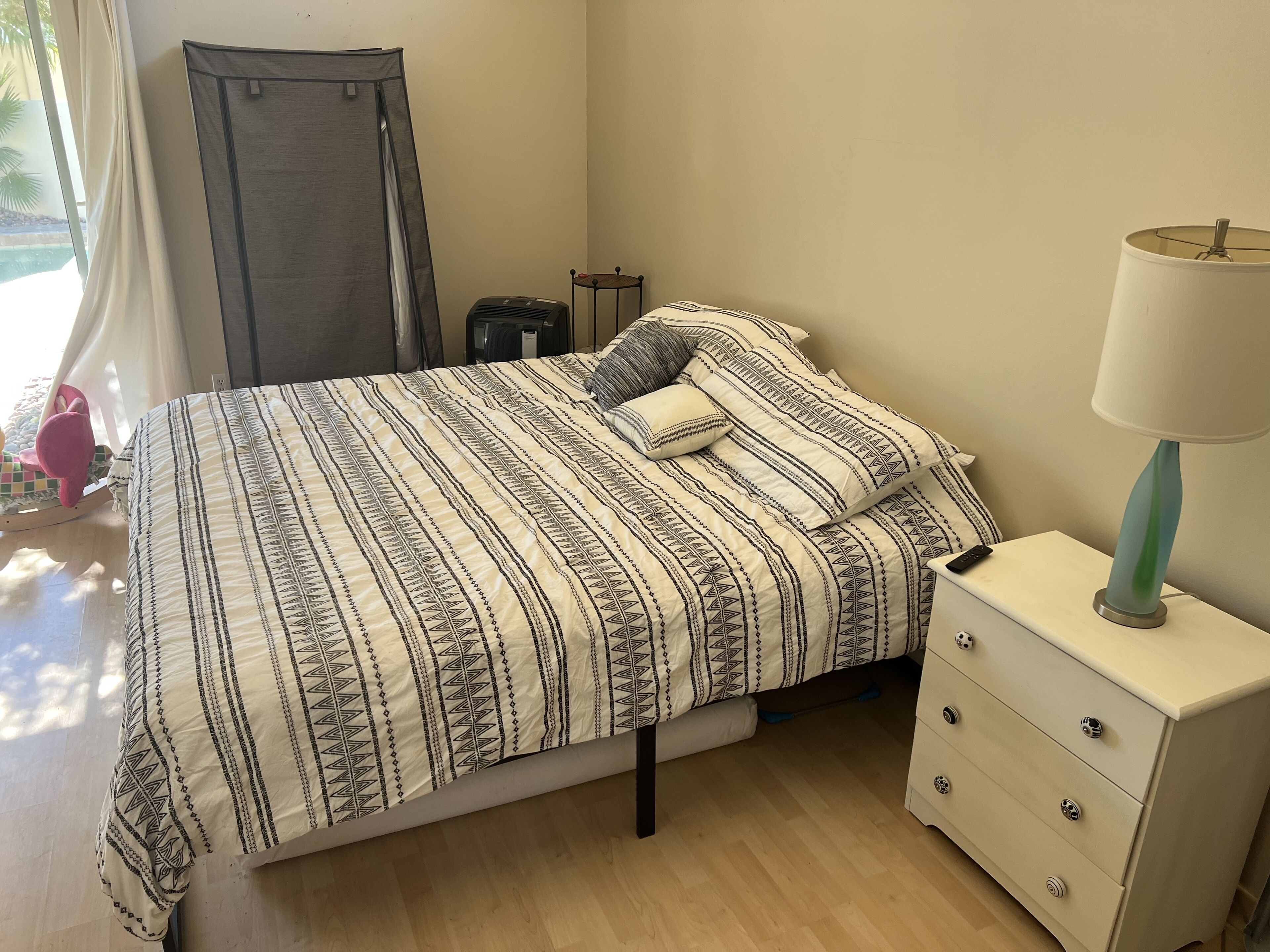 A neatly made bed with a patterned bedspread, a bedside lamp, and a small bedside table with drawers.