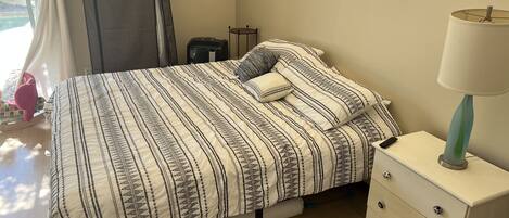 A neatly made bed with a patterned bedspread, a bedside lamp, and a small bedside table with drawers.