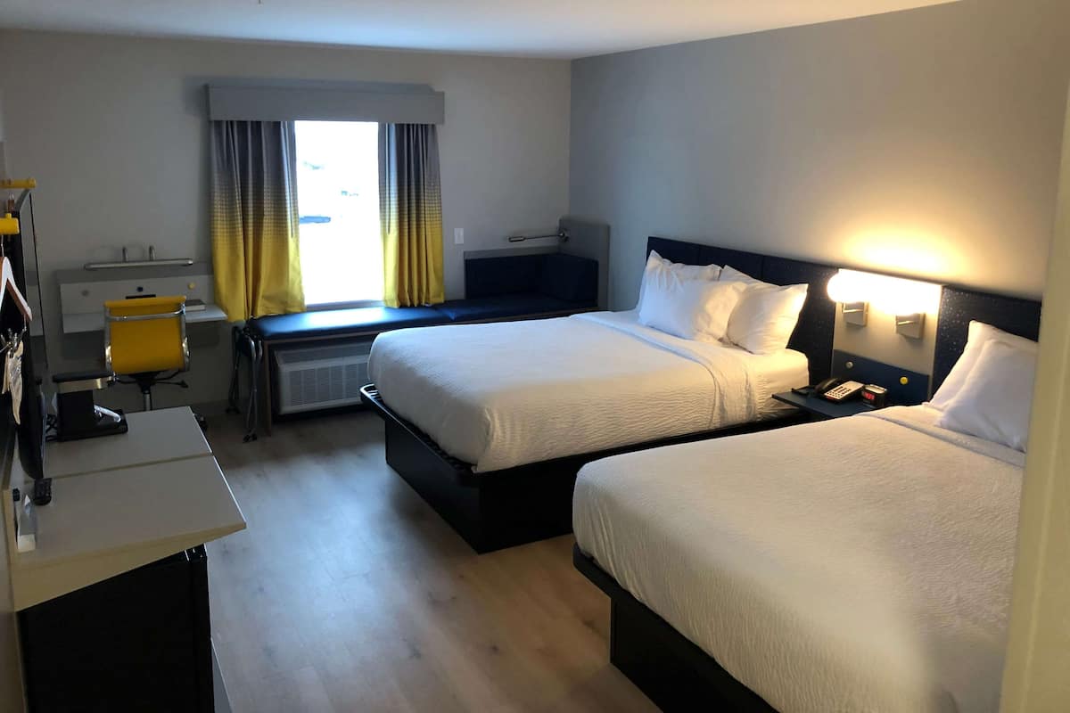 A hotel room with two beds, a desk, a chair, and a window with curtains.