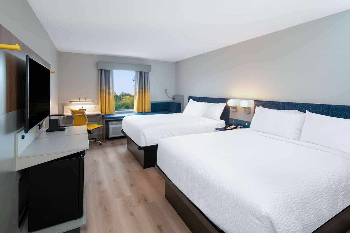 A hotel room with two beds, a desk with a computer, a TV, and a window with curtains.