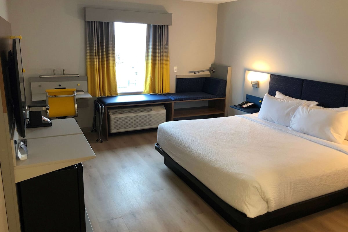 A hotel room with a bed, desk, chair, and a small seating area by the window.